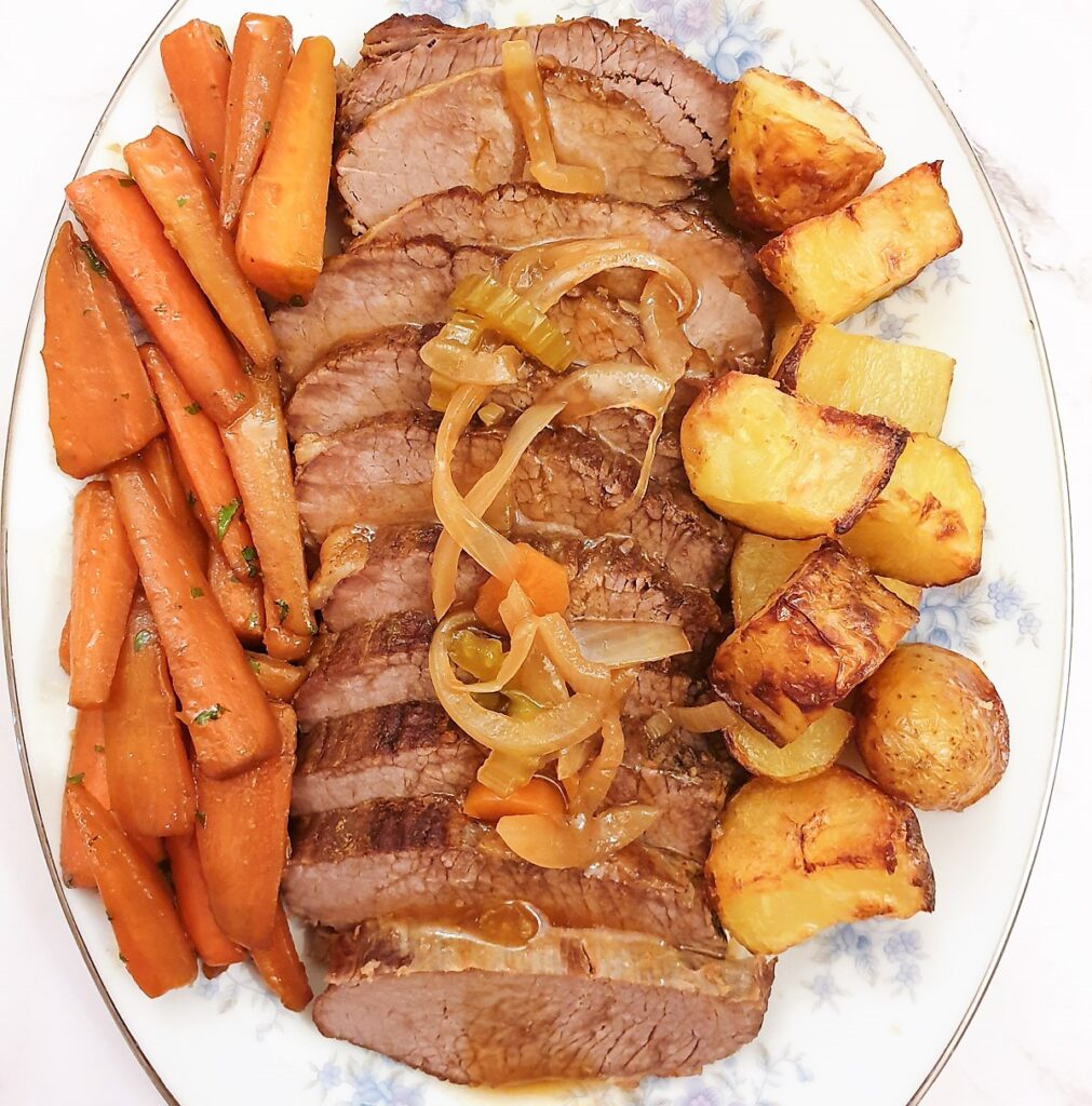 Closeup of a sliced slow-cooked silverside beef joint covered in chunky gravy.