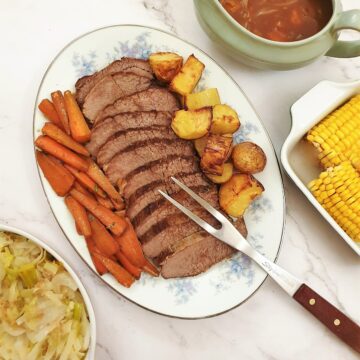 Sliced silverside on a plate with carrots and potatoes.