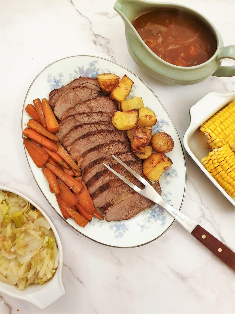 Sliced silverside on a plate with carrots and potatoes.