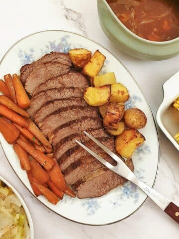 Sliced silverside on a plate with carrots and potatoes.