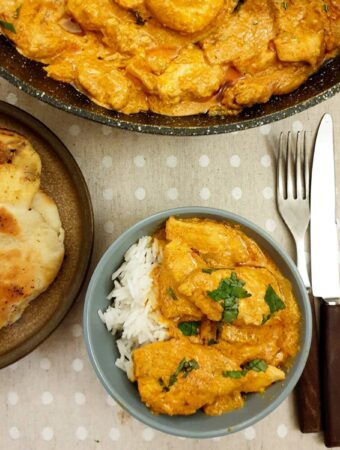 A dish of butter chicken next to a plate of garlic naan bread.