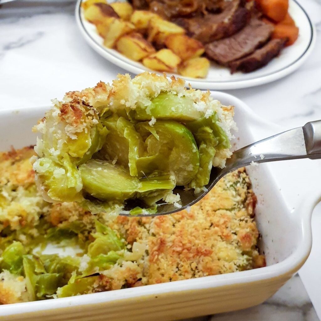 A spoonful of leek and brussels sprout bake being lifted from the serving dish.