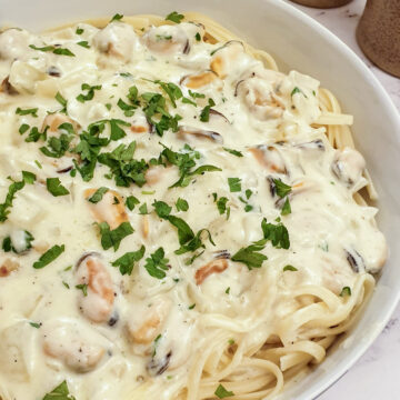 Close up view of a plate of creamy mussel pasta on a bed of linguine.