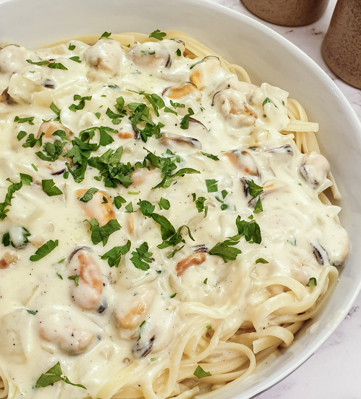 Close up view of a plate of creamy mussel pasta on a bed of linguine.