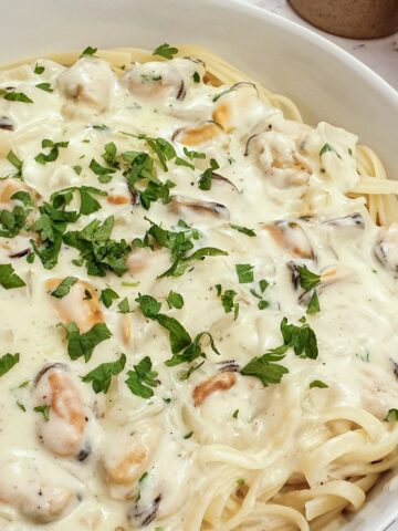 Close up view of a plate of creamy mussel pasta on a bed of linguine.