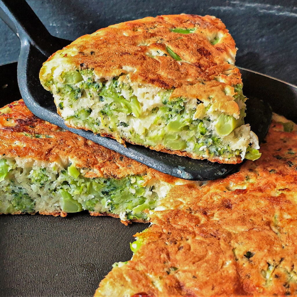 A slice of broccoli and cheese tart being lifted from the frying pan.