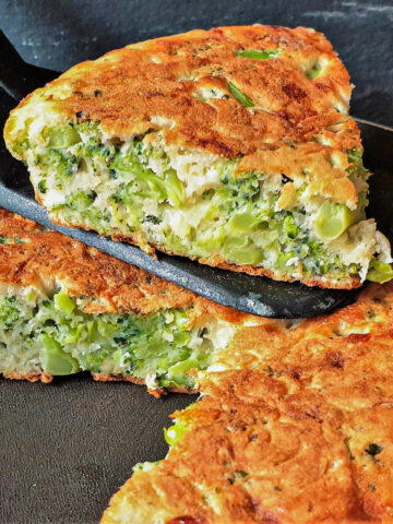 A slice of broccoli and cheese tart being lifted from the frying pan.