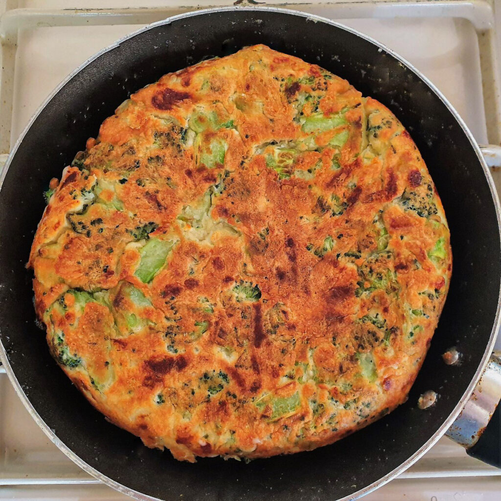 A broccoli and cheese tart turned over in the pan, showing the browned underside.