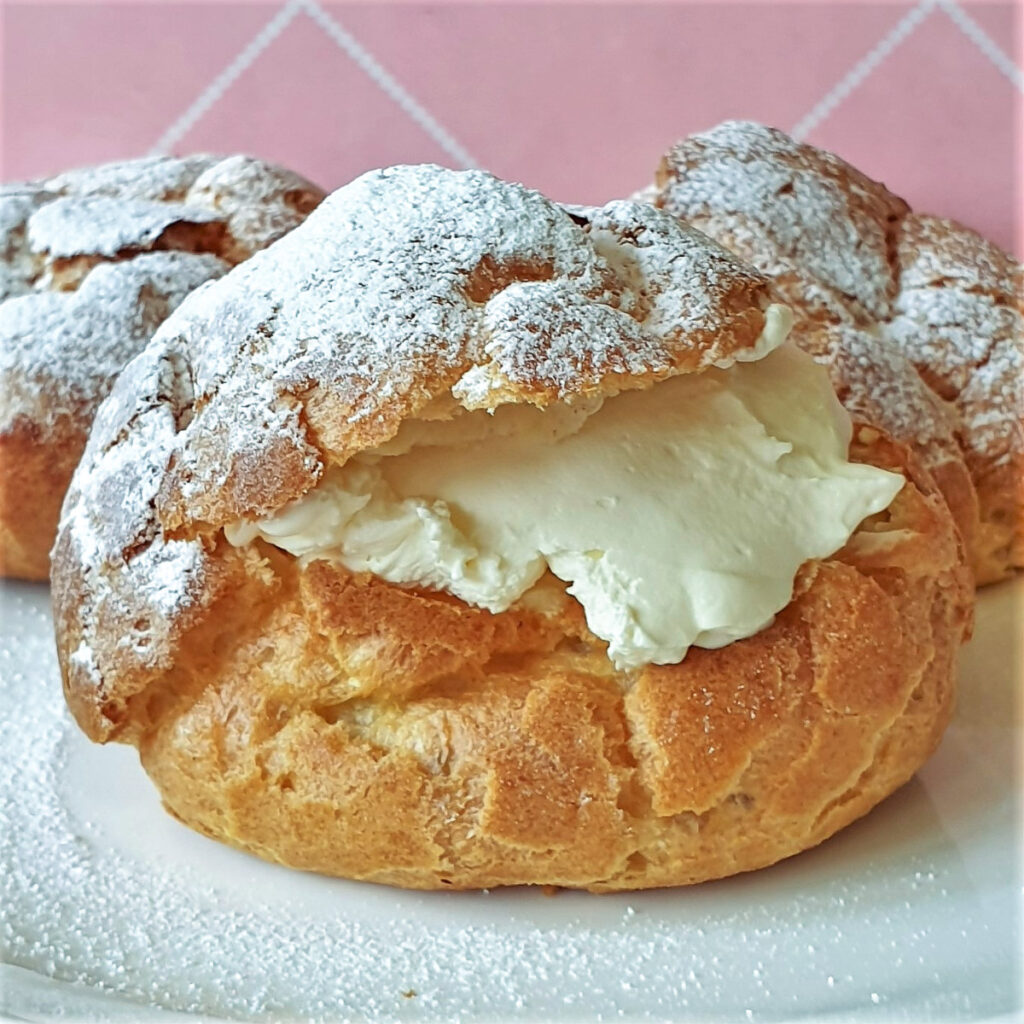 Homemad3 cream puffs filled with cream on a plate.e cream puffs. Light-as-a-feather choux pastry filled with whipped cream. Easier to make than you would think. #chouxbuns #creampuffs #chouxpastry #creampastries #eclairs 3 cream puffs filled with cream on a plate.