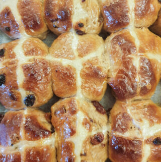 A close up of hot cross buns on a baking tray.