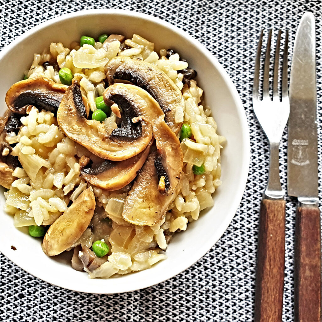 A dish of mushroom and pea risotto next to a knife and fork.