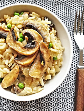 A dish of mushroom and pea risotto next to a knife and fork.