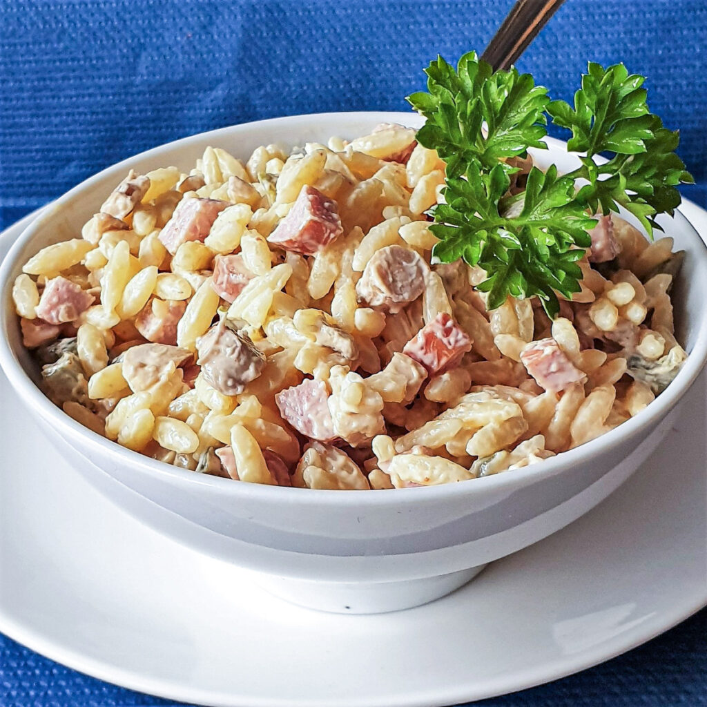 A white bowl of orzo pasta on a white plate.