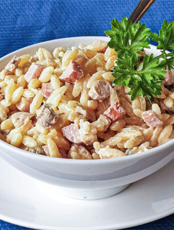 A white bowl of orzo pasta on a white plate.