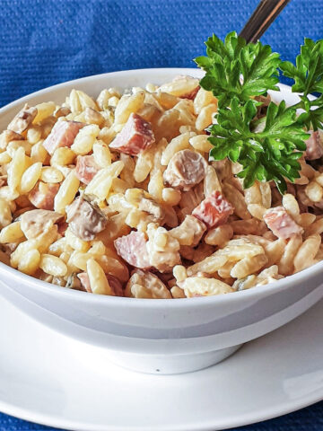 A white bowl of orzo pasta on a white plate.