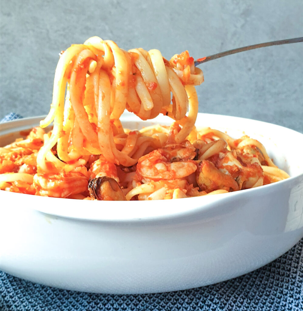 A forkful of linguine over a bowl of pasta pescatone.