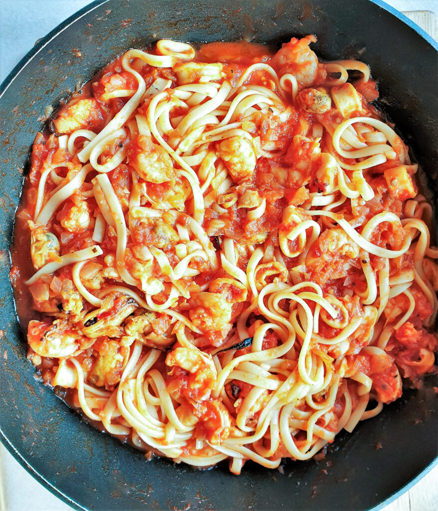 A pan of pasta pescatore sauce mixed with linguine pasta.