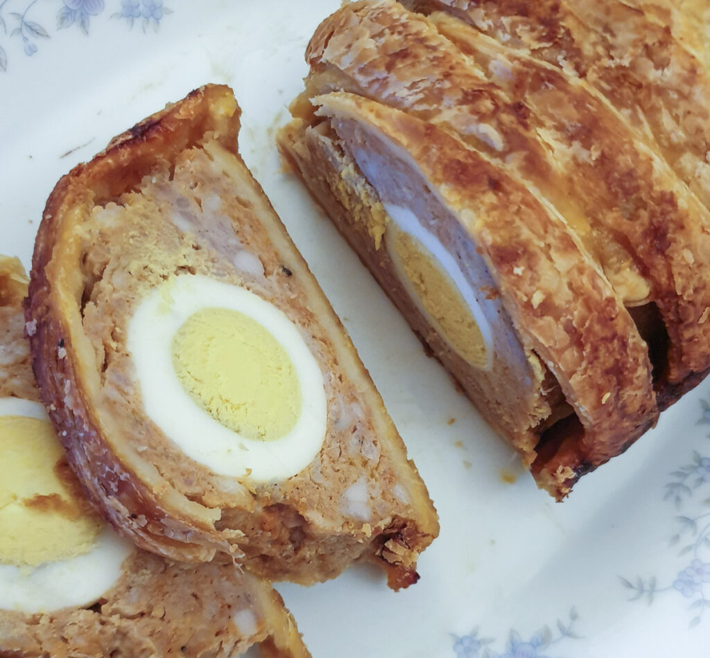 A slice of the egg filled sausage roll on a plate.