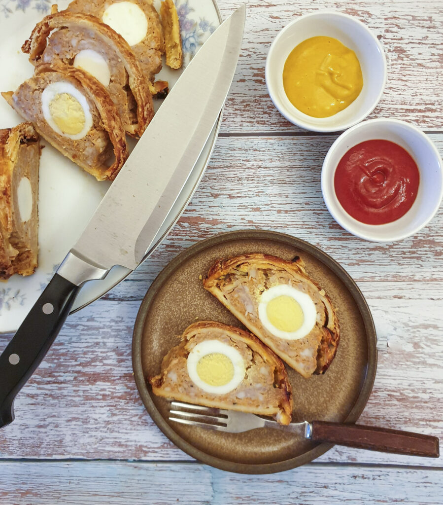 2 slices of sausage and egg roll on a plate with dishes of tomato ketchup and mustard.