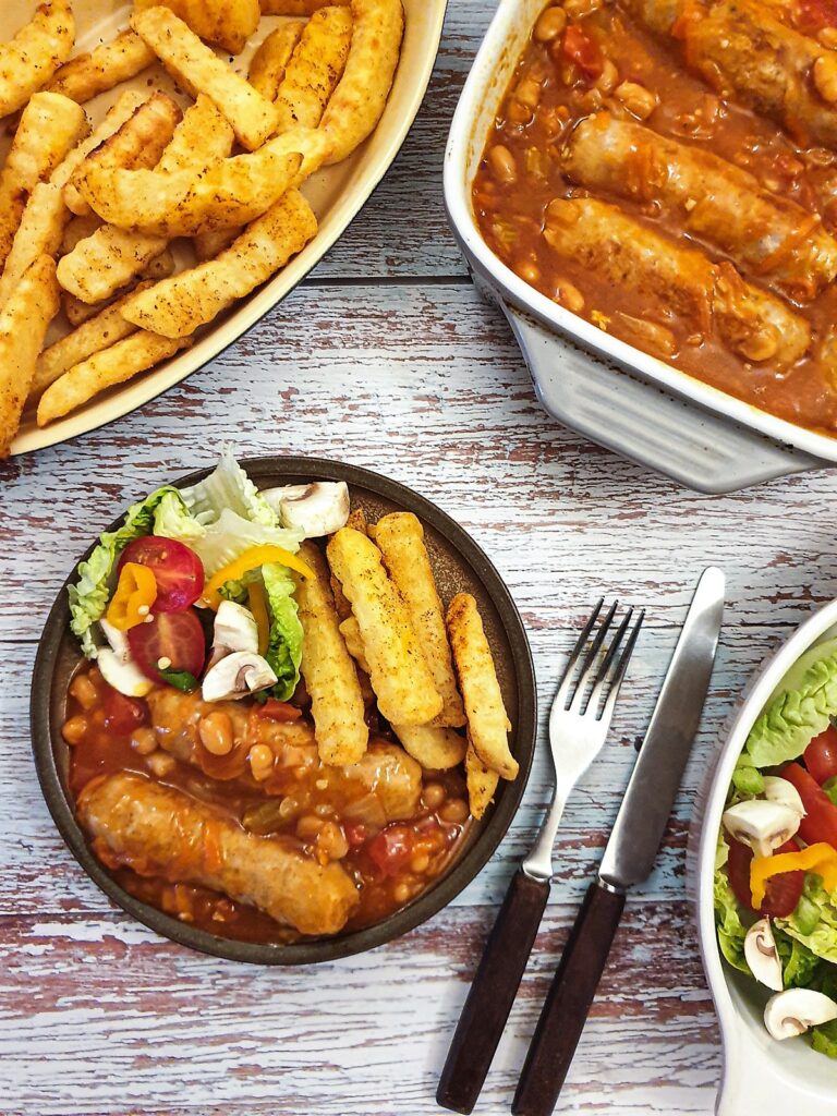 A plate containing sausages and french fries with salad.