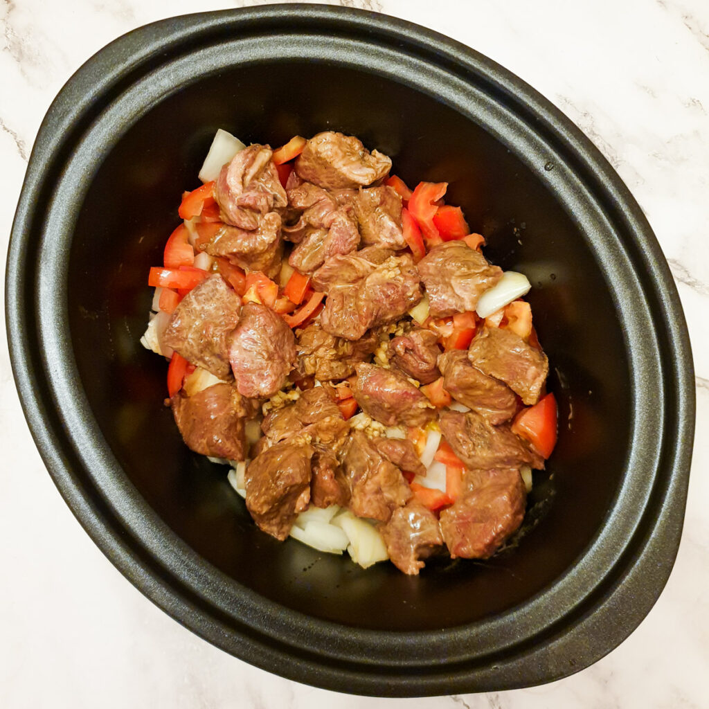 Tomatoes, onions and beef layered in a slow cooker.