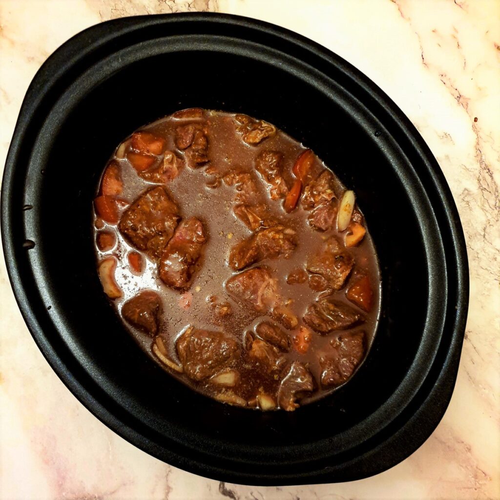 Tomatoes, onions and beef covered with gravy in a slow cooker.