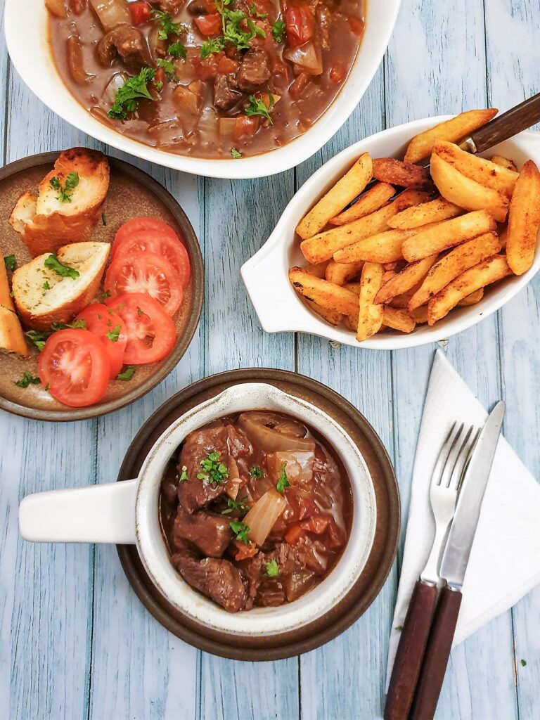 A dish of beef Trinchado alongside a bowl of french fries and garlic bread. A dish of beef Trinchado alongside a bowl of french fries and garlic bread.