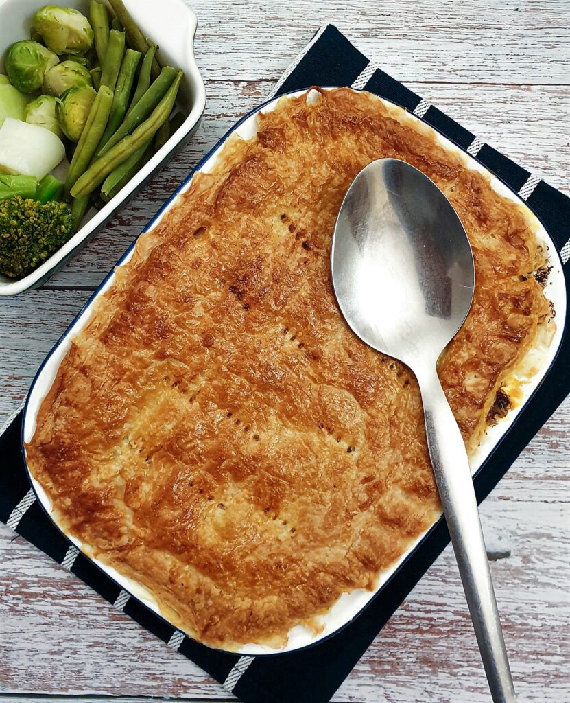 Overhead shot of a beef and mushroom pie with a serving spoon and a side dish of vegetables.