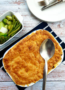 A steak and mushroom pie next to a bowl of freshly steamed vegetables.