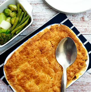 A steak and mushroom pie next to a bowl of freshly steamed vegetables.