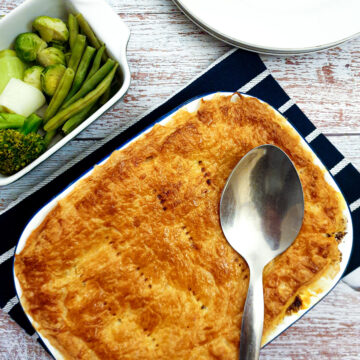 A steak and mushroom pie next to a bowl of freshly steamed vegetables.