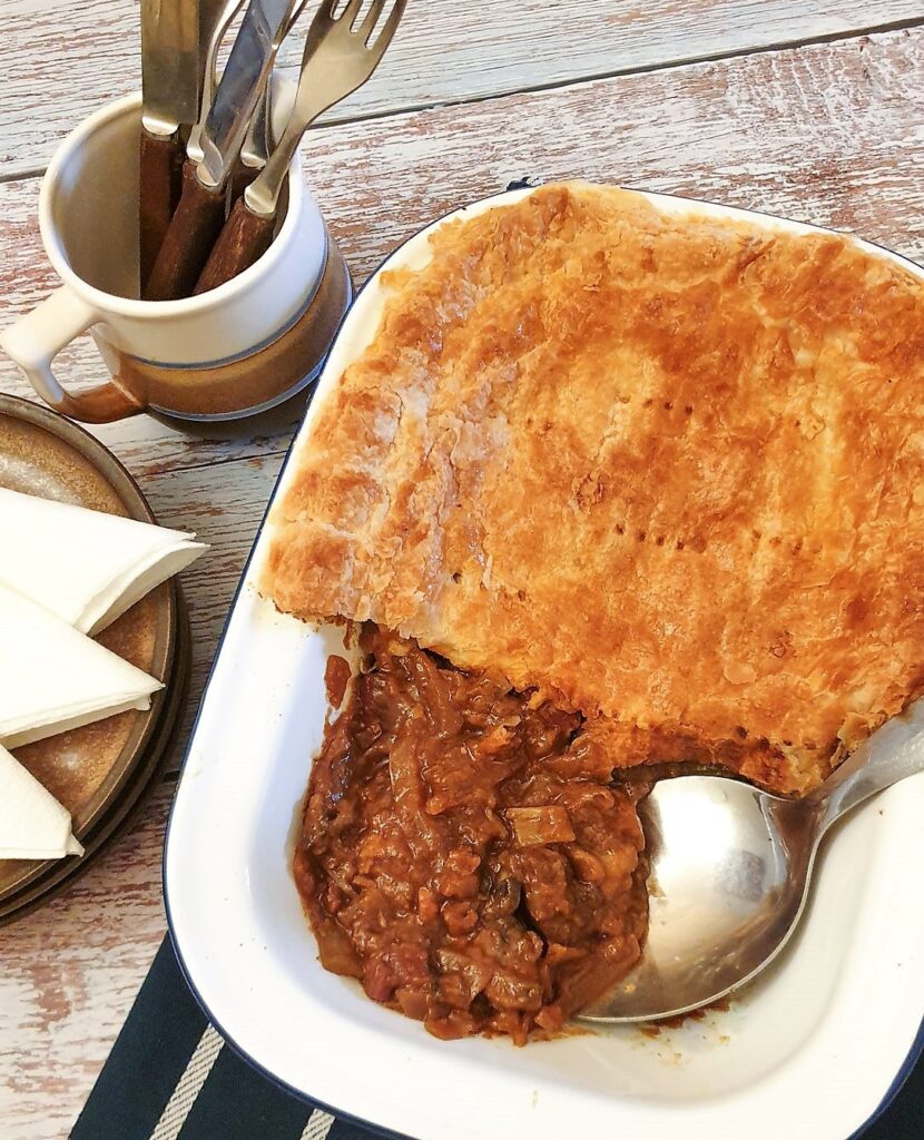 Steak and mushroom pie in a pie dish with a piece of pastry removed to show the filling.
