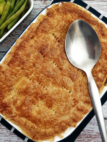 Overhead shot of a beef and mushroom pie with a serving spoon and a side dish of vegetables.