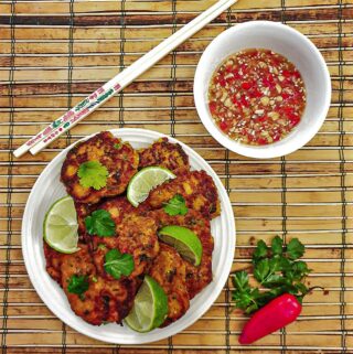 A plate of thai salmon fishcakes next to a bowl of spicy dipping sauce.