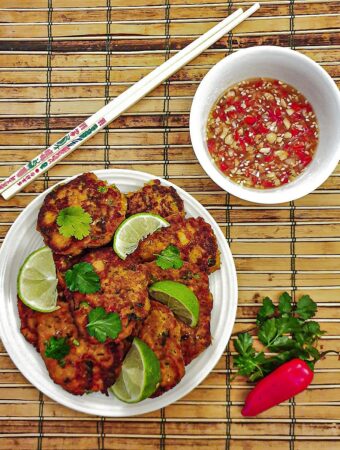 A plate of thai salmon fishcakes next to a bowl of spicy dipping sauce.