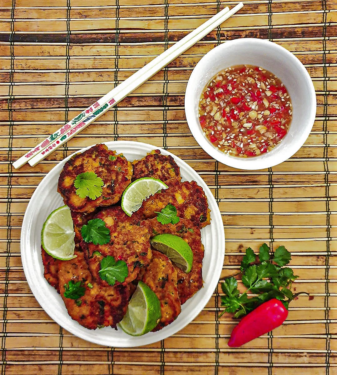 A plate of thai salmon fishcakes next to a bowl of spicy dipping sauce.
