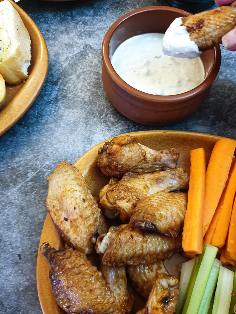 A chicken wing being dipped in blue cheese sauce, next to a plate of wings.