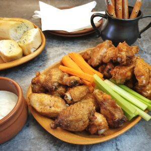 A piate of crispy air-frier crispy chicken wings on a table with carrot and celery sticks.
