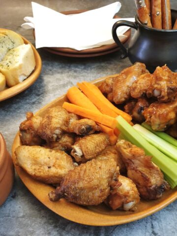 A piate of crispy air-frier crispy chicken wings on a table with carrot and celery sticks.