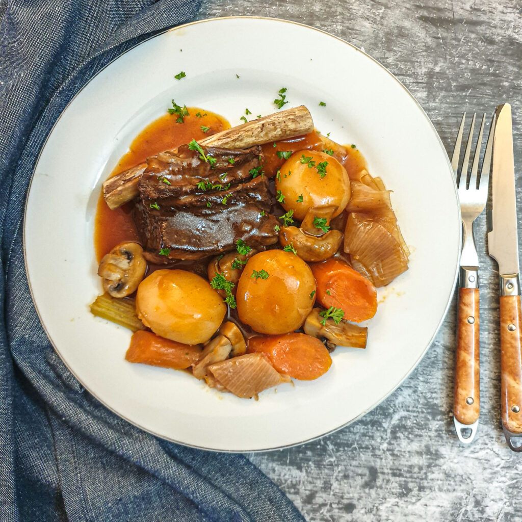 A plate of beef short rib surrounded by vegetables and covered in red wine gravy.