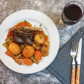 A plate of beef short rib and vegetables next to a glass of red wine