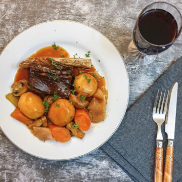A plate of beef short rib and vegetables next to a glass of red wine