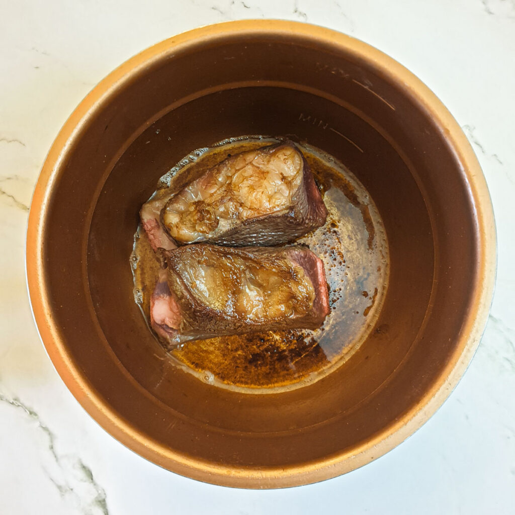 Two pieces of beef short rib browning in a pressure cooker.