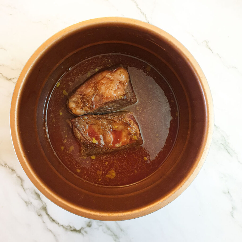 Two pieces of beef short rib in a pressure cooker, covered with stock.