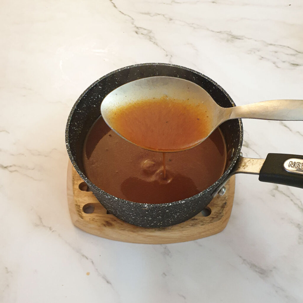 Gravy being lifted from a saucepan on a large spoon.