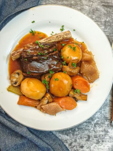 A plate of beef short rib surrounded by vegetables and covered in red wine gravy.