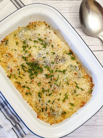 A dish of cauliflower and broccoli cheese sprinkled with chopped chives.