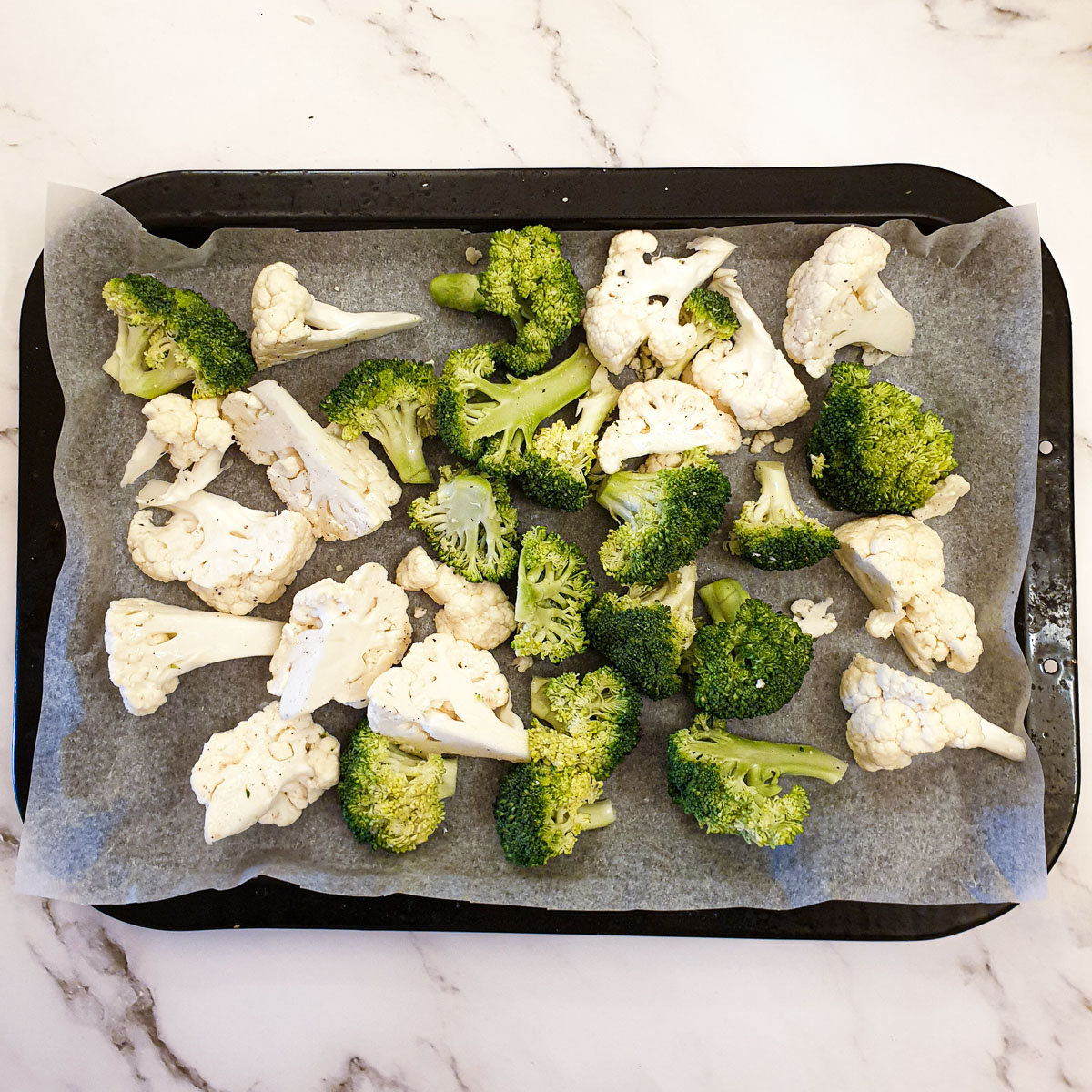 Raw cauliflower and broccoli florets on a baking sheet.