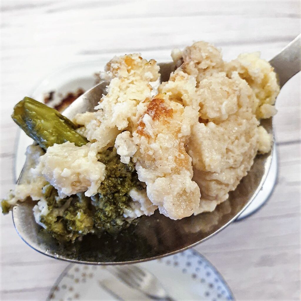 Close up of a helping of cauliflower and broccoli cheese on a serving spoon.