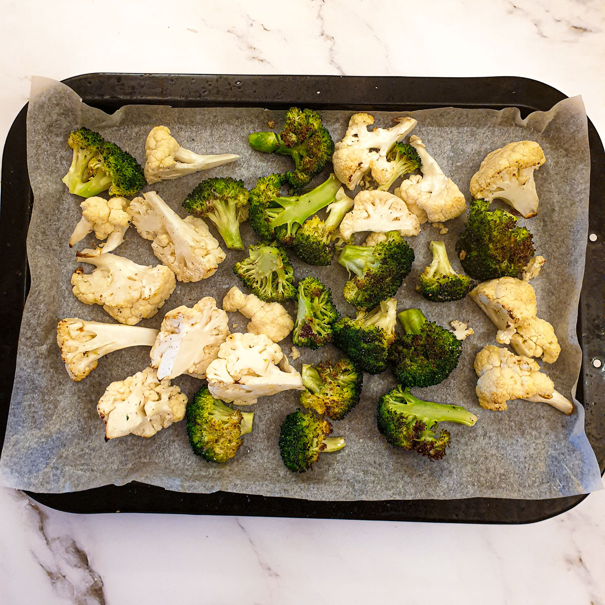 Cauliflower and broccoli florets on a baking sheet once they have browned in the oven.